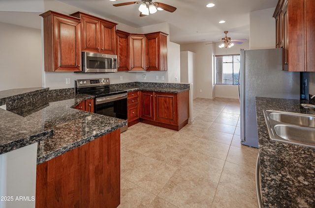 kitchen with recessed lighting, stainless steel appliances, a peninsula, a sink, and dark stone countertops