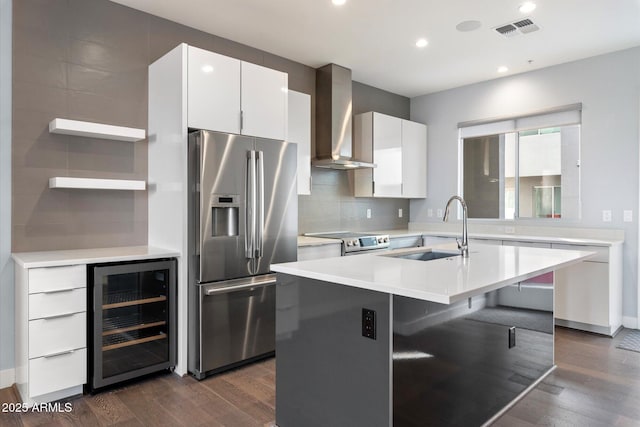 kitchen featuring sink, wall chimney exhaust hood, an island with sink, wine cooler, and appliances with stainless steel finishes