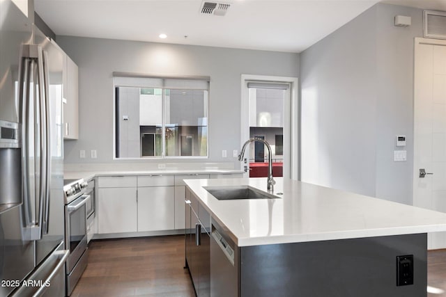 kitchen featuring sink, stainless steel appliances, white cabinetry, and a center island with sink