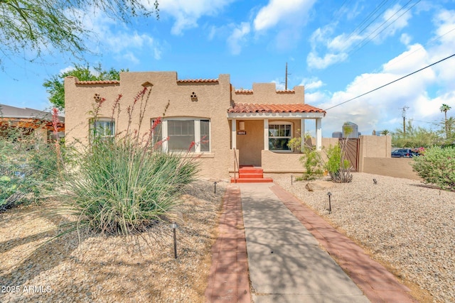 mediterranean / spanish-style house featuring stucco siding, a tiled roof, a gate, and fence