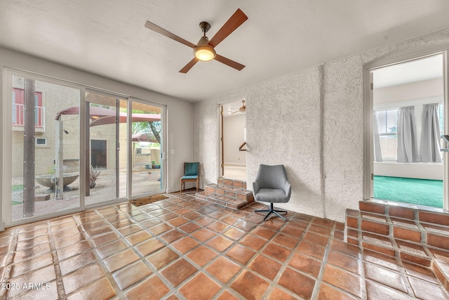 living area with a ceiling fan and a textured wall