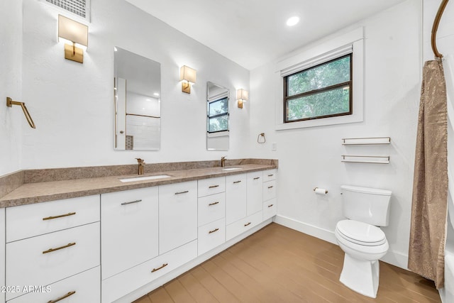 full bath featuring toilet, wood finished floors, double vanity, and baseboards