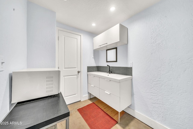 bathroom with a textured wall, baseboards, recessed lighting, vanity, and tasteful backsplash
