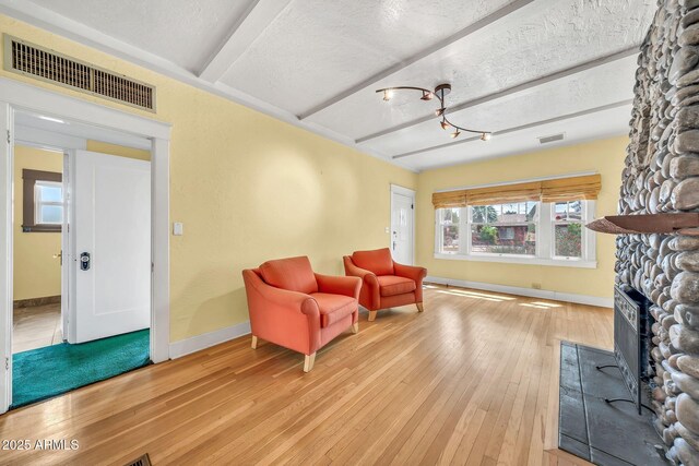 living area featuring baseboards, hardwood / wood-style flooring, a stone fireplace, beamed ceiling, and a chandelier