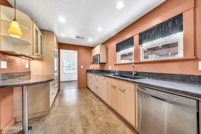 kitchen featuring stainless steel appliances, a sink, dark countertops, recessed lighting, and decorative light fixtures
