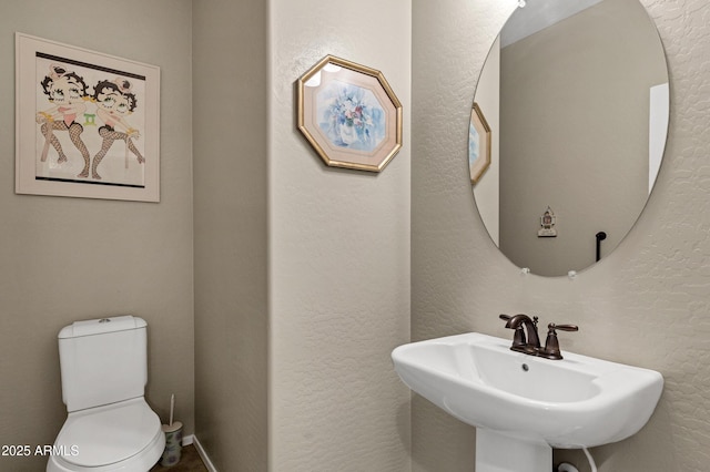 bathroom with a textured wall, a sink, and toilet