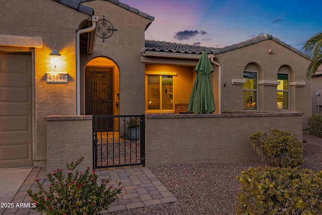 view of front of home featuring a fenced front yard, an attached garage, a tile roof, a gate, and stucco siding