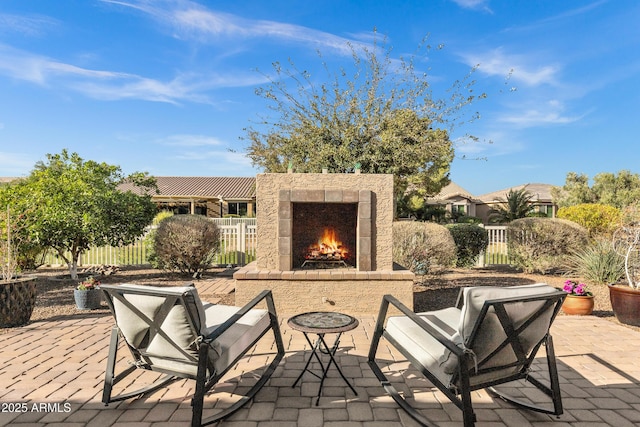 view of patio with a warm lit fireplace and fence