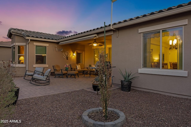 back of house at dusk featuring stucco siding, an outdoor hangout area, a patio area, ceiling fan, and a tiled roof