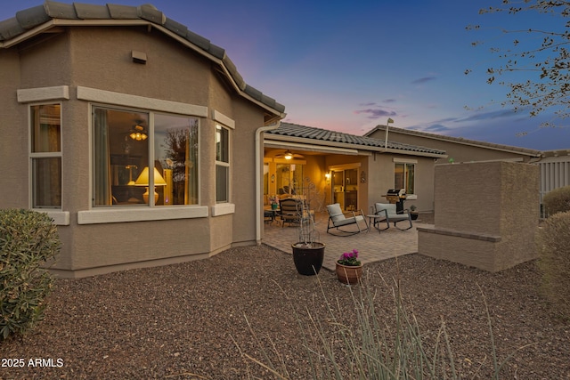 rear view of house featuring a patio area, a tile roof, and stucco siding