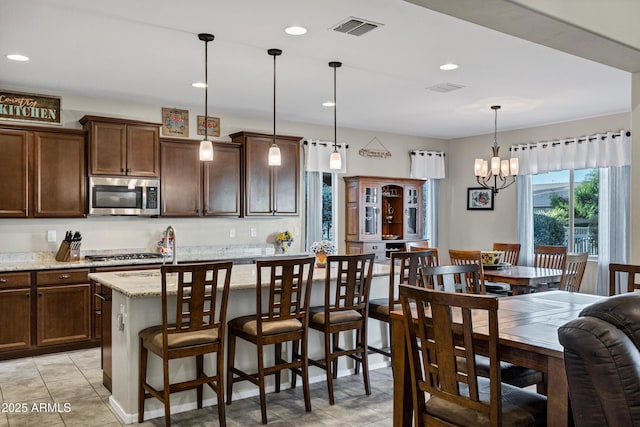 kitchen featuring stainless steel appliances, visible vents, dark brown cabinetry, and light stone countertops