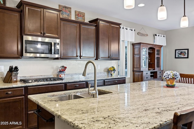 kitchen with dark brown cabinetry, an island with sink, appliances with stainless steel finishes, light stone countertops, and a sink