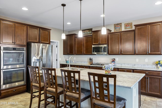 kitchen featuring dark brown cabinetry, a center island with sink, stainless steel appliances, pendant lighting, and a sink