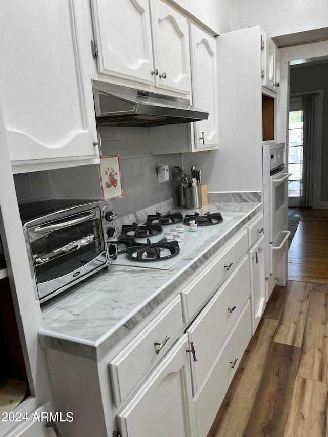 kitchen with wood-type flooring, white gas cooktop, white cabinetry, backsplash, and stainless steel oven