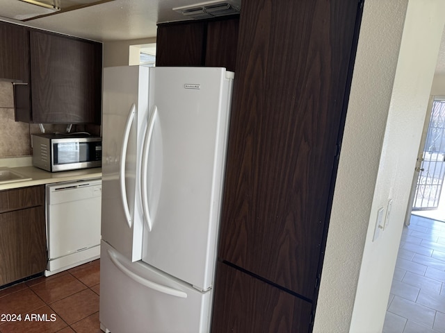 kitchen with dark brown cabinets, white appliances, dark tile patterned flooring, and sink