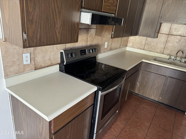 kitchen with stainless steel electric stove, sink, dark tile patterned floors, tasteful backsplash, and dark brown cabinetry