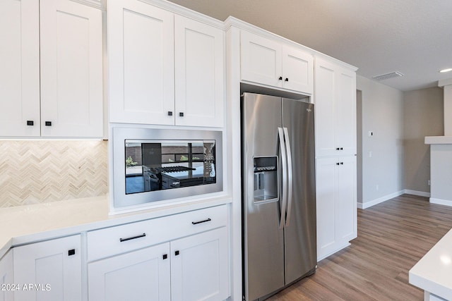 kitchen with light hardwood / wood-style floors, built in microwave, stainless steel refrigerator with ice dispenser, white cabinetry, and backsplash