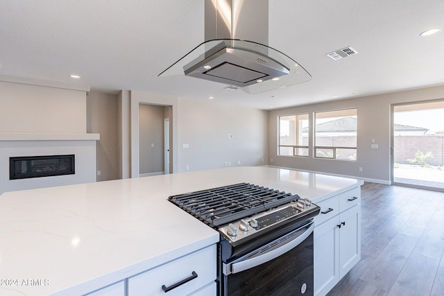 kitchen featuring white cabinets, light stone counters, wood-type flooring, island range hood, and stainless steel range with gas stovetop