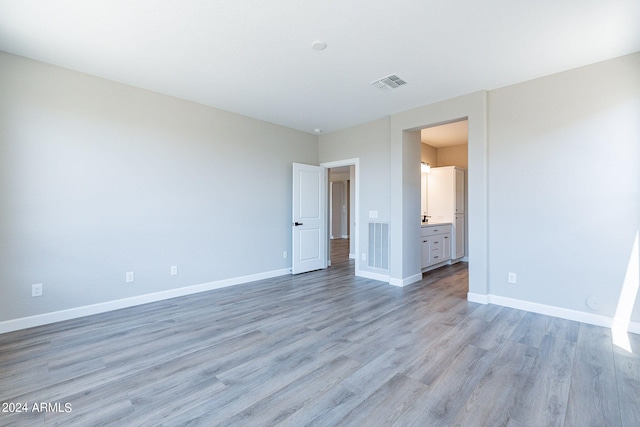 unfurnished bedroom with ensuite bath and light wood-type flooring