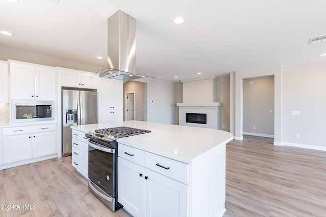 kitchen with a large fireplace, island range hood, a center island, white cabinetry, and appliances with stainless steel finishes