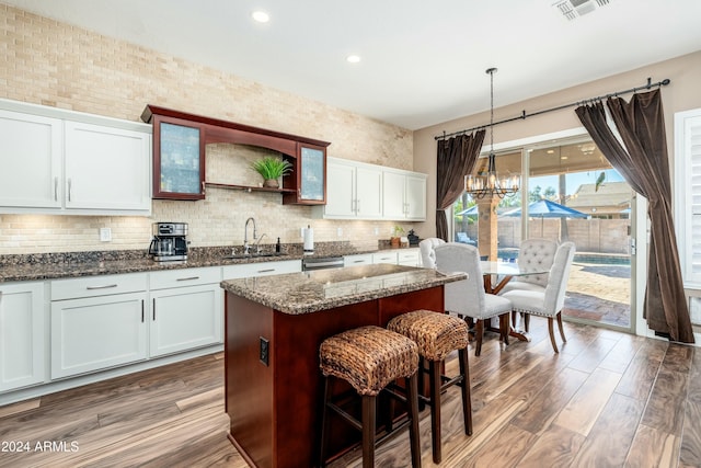 kitchen featuring sink, decorative light fixtures, white cabinetry, a center island, and dark stone countertops