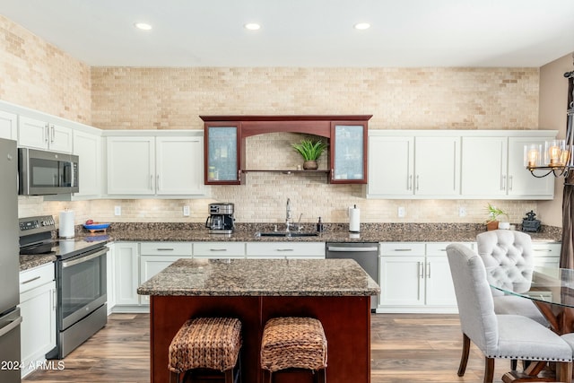 kitchen with sink, decorative light fixtures, dark stone counters, a kitchen island, and appliances with stainless steel finishes