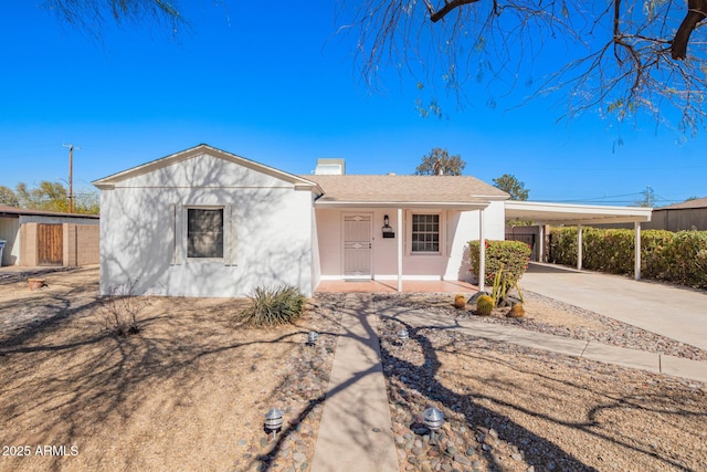 ranch-style home featuring a chimney, stucco siding, concrete driveway, covered porch, and a carport