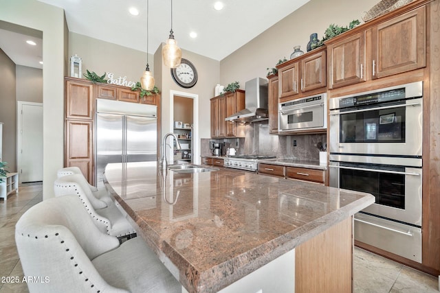 kitchen featuring a kitchen bar, wall chimney range hood, appliances with stainless steel finishes, and a large island