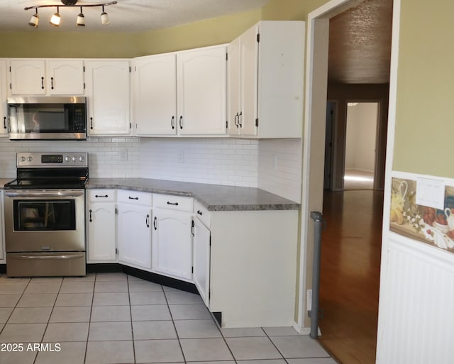 kitchen with light tile patterned floors, stainless steel appliances, backsplash, and white cabinets