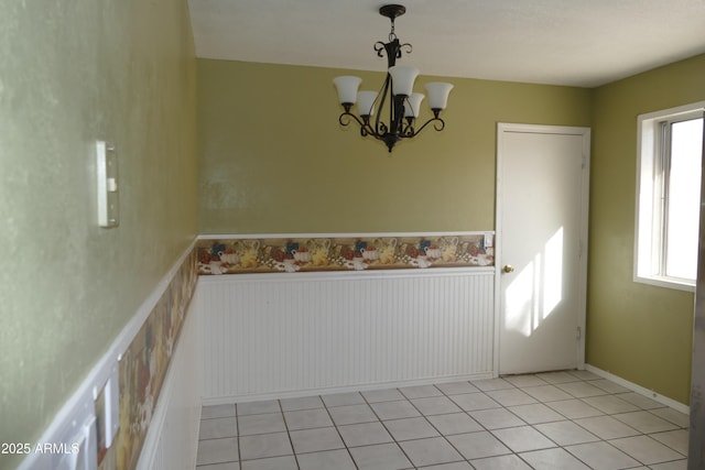 unfurnished dining area featuring a wainscoted wall, light tile patterned floors, and an inviting chandelier