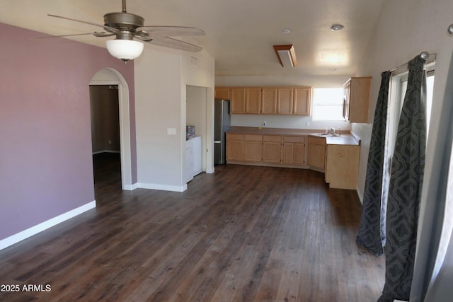 kitchen featuring arched walkways, light brown cabinets, a sink, freestanding refrigerator, and dark wood-style floors