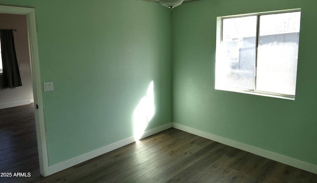 spare room featuring dark wood-type flooring, a wealth of natural light, and baseboards