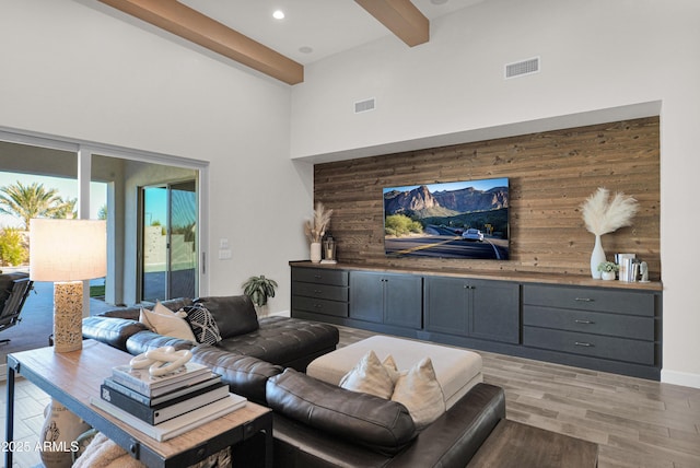 living room featuring light hardwood / wood-style flooring, a towering ceiling, beamed ceiling, and wooden walls