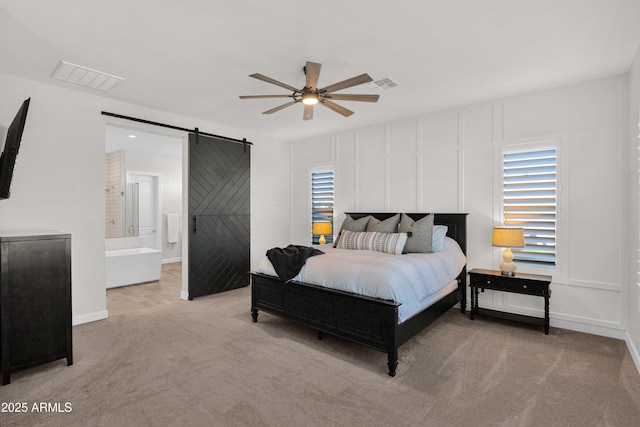 carpeted bedroom with ensuite bath, ceiling fan, and a barn door