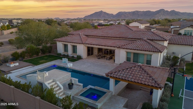 back house at dusk featuring a pool with hot tub, a mountain view, and a patio