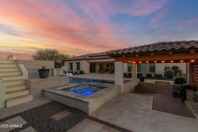 pool at dusk with an in ground hot tub, a patio area, and area for grilling