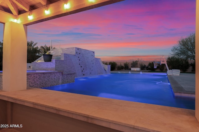 pool at dusk featuring pool water feature and a bar