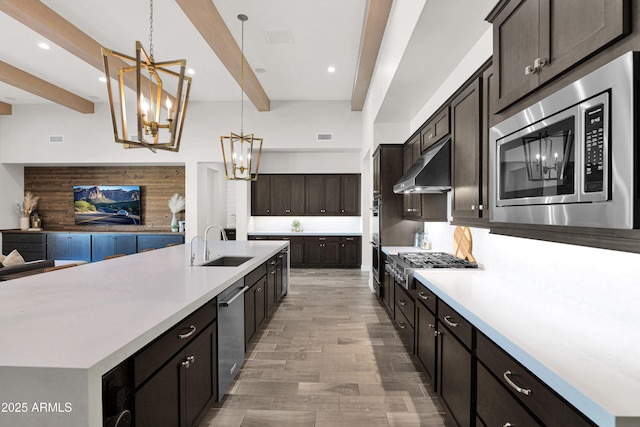 kitchen with pendant lighting, appliances with stainless steel finishes, wall chimney range hood, sink, and beam ceiling