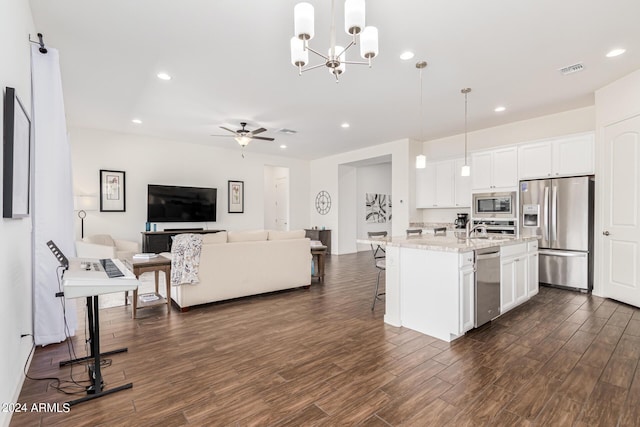 kitchen with dark wood finished floors, white cabinets, appliances with stainless steel finishes, a kitchen breakfast bar, and open floor plan