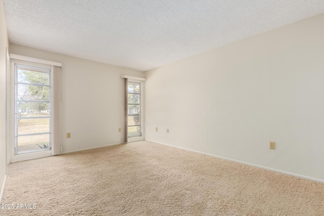 carpeted spare room with plenty of natural light, a textured ceiling, and baseboards