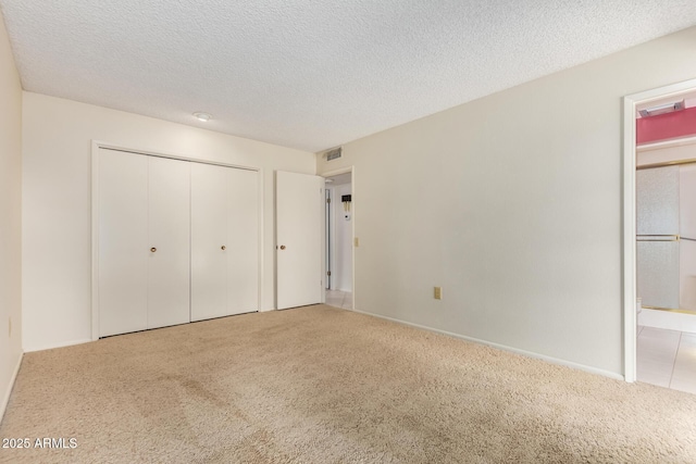 unfurnished bedroom with a textured ceiling, a closet, carpet, and visible vents