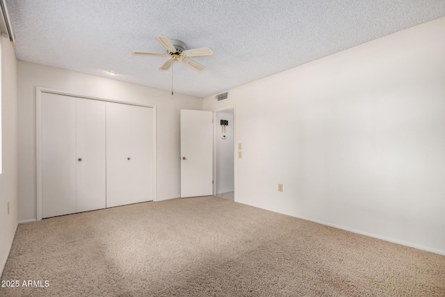 unfurnished bedroom with a textured ceiling, carpet floors, visible vents, a ceiling fan, and a closet