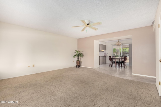 carpeted empty room with a textured ceiling, ceiling fan with notable chandelier, and tile patterned flooring