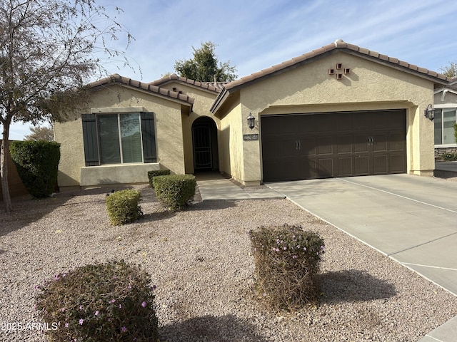 mediterranean / spanish-style house featuring an attached garage, a tiled roof, concrete driveway, and stucco siding