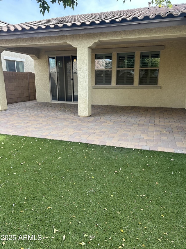 rear view of property with a tiled roof, a patio area, fence, and stucco siding