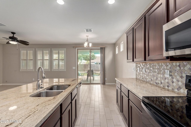 kitchen with light stone counters, stainless steel appliances, visible vents, decorative backsplash, and a sink