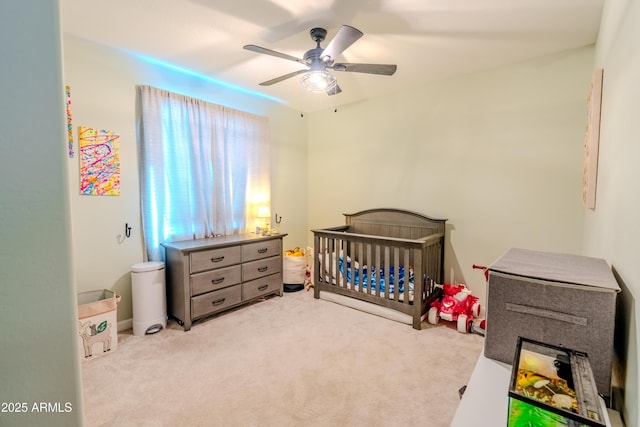 carpeted bedroom featuring ceiling fan and a nursery area