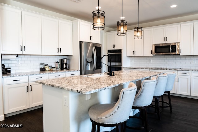 kitchen with a center island with sink, white cabinets, decorative light fixtures, and appliances with stainless steel finishes