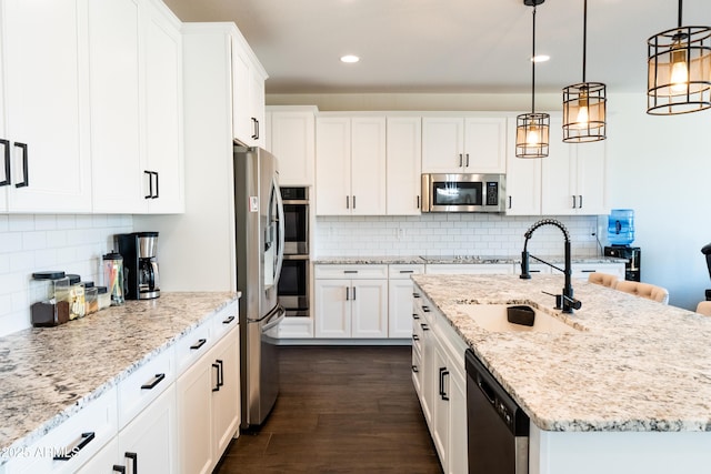 kitchen with a kitchen island with sink, white cabinets, decorative light fixtures, and appliances with stainless steel finishes