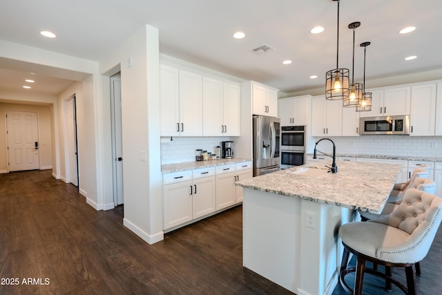 kitchen featuring sink, pendant lighting, a kitchen island with sink, white cabinets, and appliances with stainless steel finishes